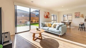 A spacious living area with a sofa, coffee table, and dining table, large sliding glass doors to a backyard, and artwork on the walls. - Modern new Homly House at Clyde (Clyde)