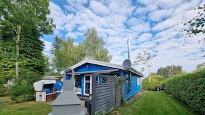 Une maison bleue avec une antenne parabolique, un barbecue et un petit abri de jardin.