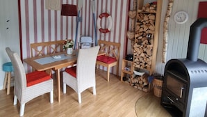Une pièce chaleureuse avec un papier peint à rayures, une table à manger en bois avec des chaises, un petit coin cuisine avec une cuisinière et une cheminée.