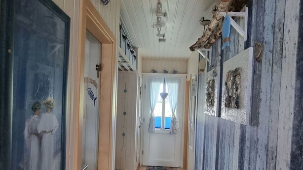 Un couloir doté d’un sol carrelé, de portes blanches et offrant une vue sur une pièce avec une fenêtre et des rideaux.