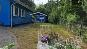 Une maison bleue avec un petit porche et un jardin agrémenté d’une chaise en métal et d’un panneau indiquant « Moulin ».