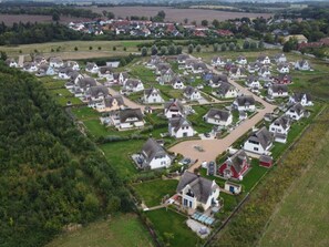 An aerial view of a residential area with houses arranged in a grid pattern, surrounded by greenery and fields.