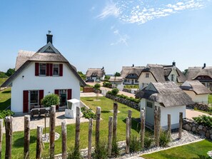 A village with traditional thatched-roof houses, a white building with red shutters, and a wooden fence.