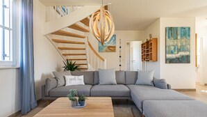 Een moderne woonkamer met een grijze modulaire bank, een houten salontafel en een trap met houten leuningen.