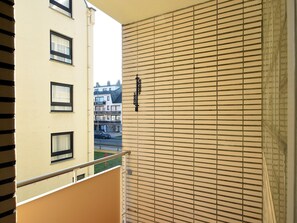 A balcony with horizontal blinds, a metal railing, and a view of neighboring buildings.