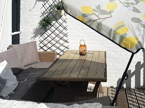 A wicker sofa, a small table, and a hanging plant against a white wall.