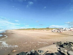 A beach with a rocky foreground, a sandy shore, and white buildings in the background.