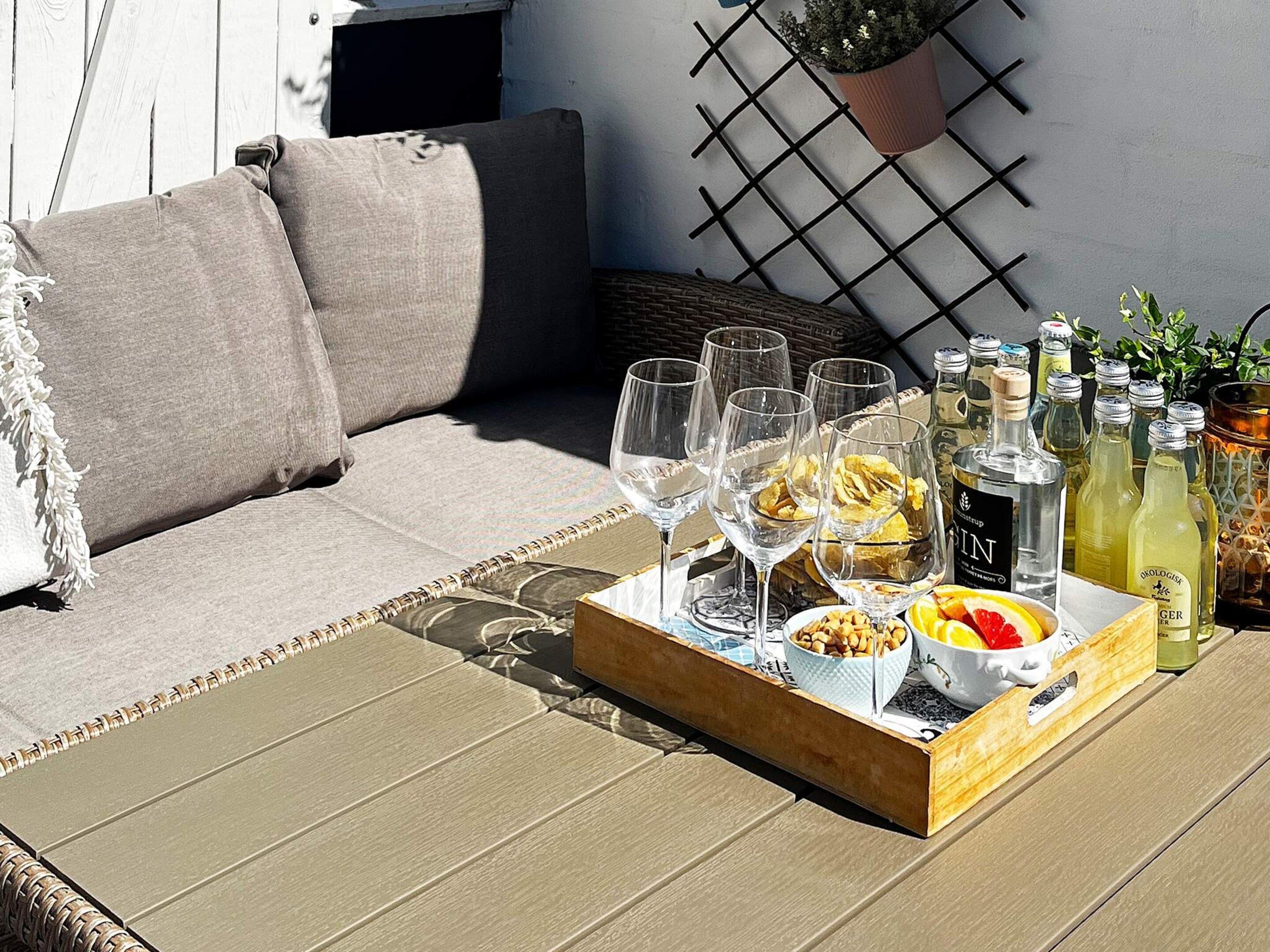 En træbakke med glas, flasker og snacks på en dæk.