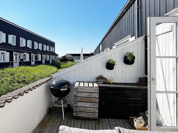 A balcony with a barbecue grill, potted plants, and a wooden bench.