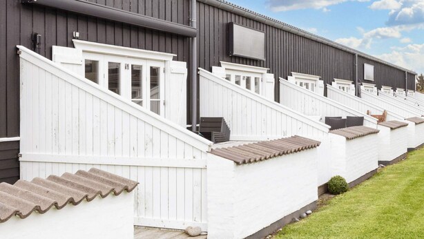 A row of white cabins with grey roofs and a grey building in the background.