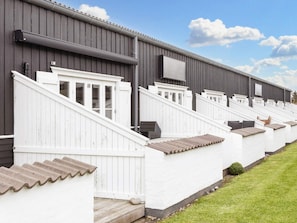 A row of white cabins with grey roofs and a grey building in the background. - 6 Person Holiday Home in Vestervig (Vestervig)
