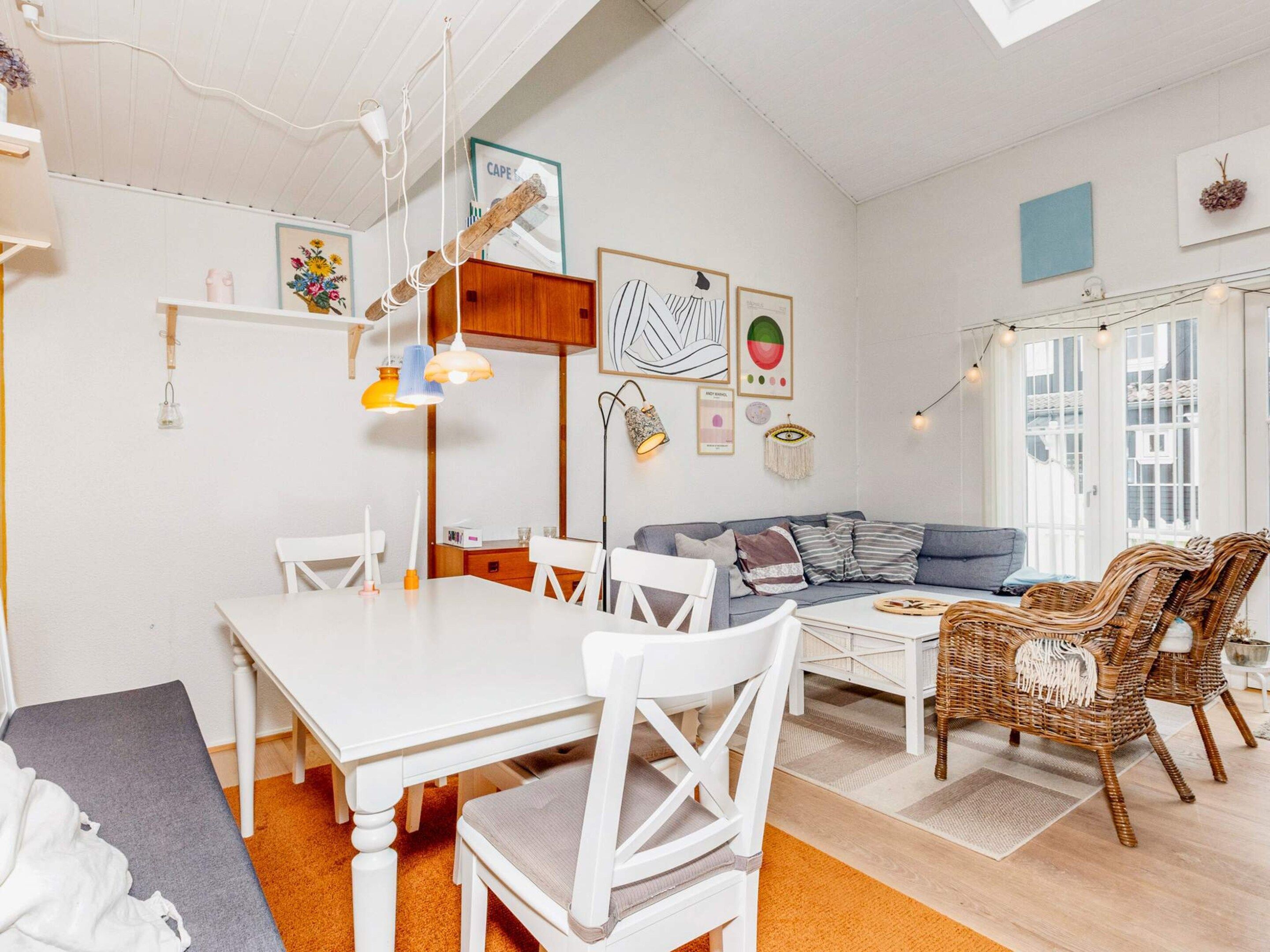 Una habitación luminosa y bien iluminada con una mesa de comedor, sillas, un sofá y sillones de mimbre.