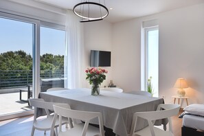 A modern dining area with a table set for four, a vase of flowers, and a flat-screen TV on the wall.