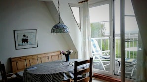 A dining area with a table set for two, a wooden bench, and a view of the outdoors through a sliding glass door. - Lagoon on the Wadden See on Wangerooge (Wangerooge)
