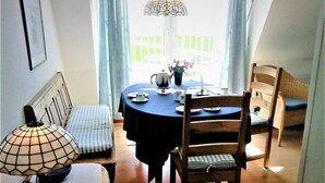 A dining area with a round table, chairs, a bench, a lamp, and a view of the outdoors. - Lagoon on the Wadden See on Wangerooge (Wangerooge)