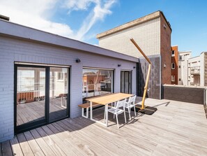 Une terrasse sur le toit avec une plateforme en bois, une table et des chaises, et une grande fenêtre.