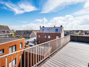 Une terrasse sur le toit avec une plateforme en bois, des bâtiments en briques et un ciel bleu dégagé.