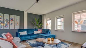 A modern living room with a blue sectional sofa, a round coffee table, and a large plant.