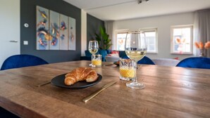 A dining table with a croissant, two glasses of white wine, and a glass of orange juice.