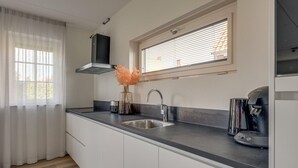 A modern kitchen with a stainless steel sink, a black range hood, and a window with blinds.