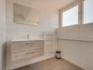 A modern bathroom with a white vanity, a mirror, a towel rack, and a window.
