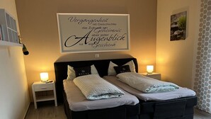 A double bed with two pillows, a bedside table with a lamp, and a wall-mounted sign with text.