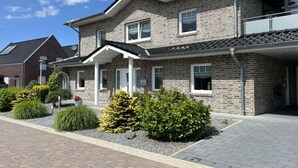 A two-story brick house with a covered porch, a small garden with shrubs and flowers, and a paved driveway.
