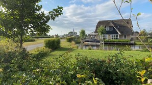 A house with a thatched roof, a pond, and a grassy area with bushes. - Villa by Tjeukemeer With Sauna & Whirlpool (Delfstrahuizen)