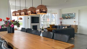 A modern living room with a wooden dining table, black leather chairs, a grey sofa, and a flat-screen TV. - Villa by Tjeukemeer With Sauna & Whirlpool (Delfstrahuizen)