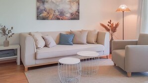 A modern living room with a beige sofa, two white side tables, a floor lamp, and a large abstract painting on the wall. - Holiday Apartment Am Buchbuhl (Stockach)