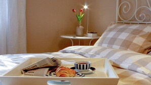 A neatly made bed with a checkered pillowcase, a tray with croissants and a cup of coffee, and a vase with tulips on a bedside table. - Holiday Apartment Am Buchbuhl (Stockach)