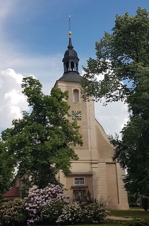 A church with a tall bell tower, surrounded by lush greenery and flowering bushes. - Tasteful Apartment in Burg (Burg (Spreewald))