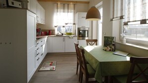 A compact kitchen with white cabinets, a wooden ceiling, and a dining area with a green tablecloth. - Tasteful Apartment in Burg (Burg (Spreewald))