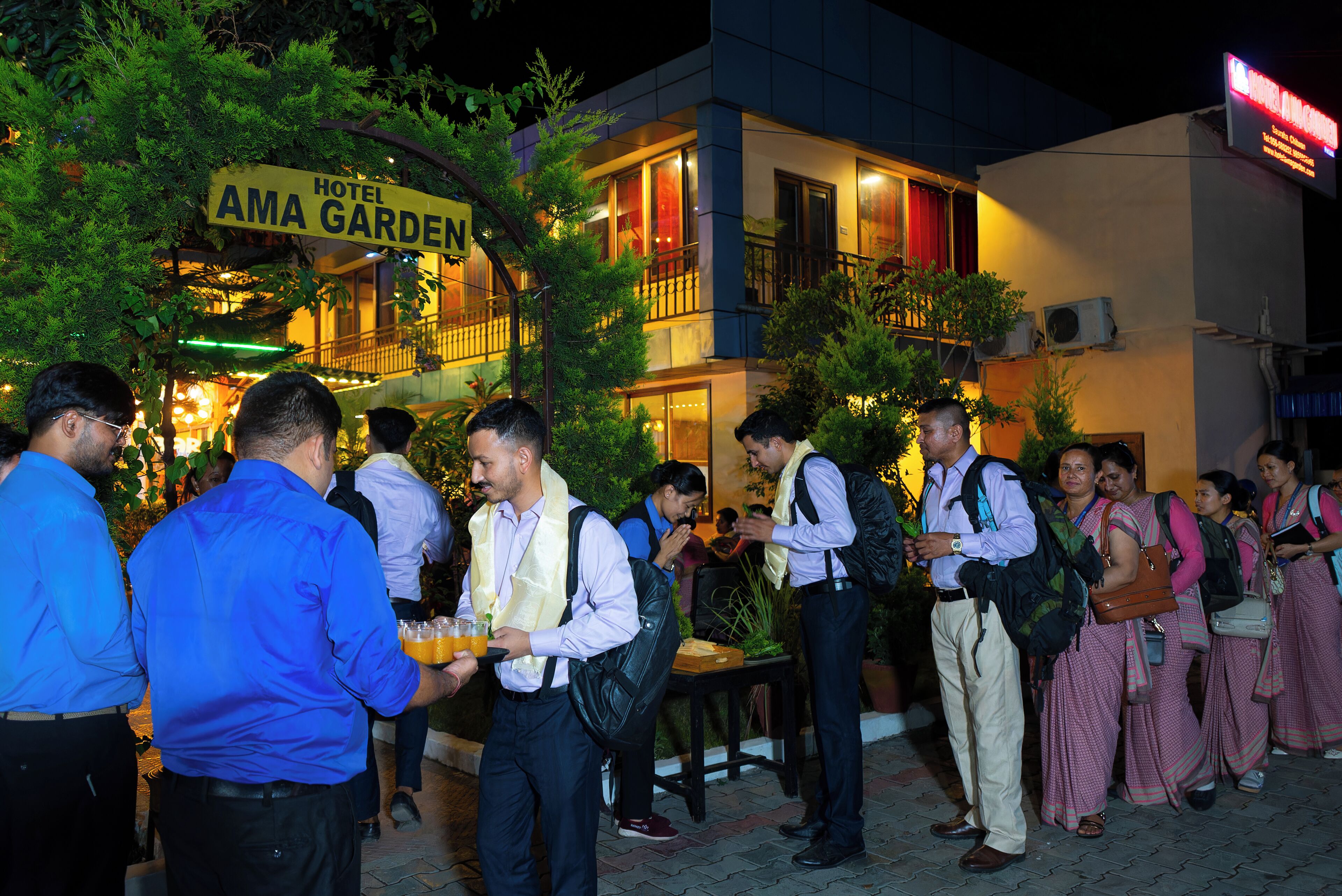 A hotel named "AMA GARDEN" with a signboard, surrounded by guests and greenery.