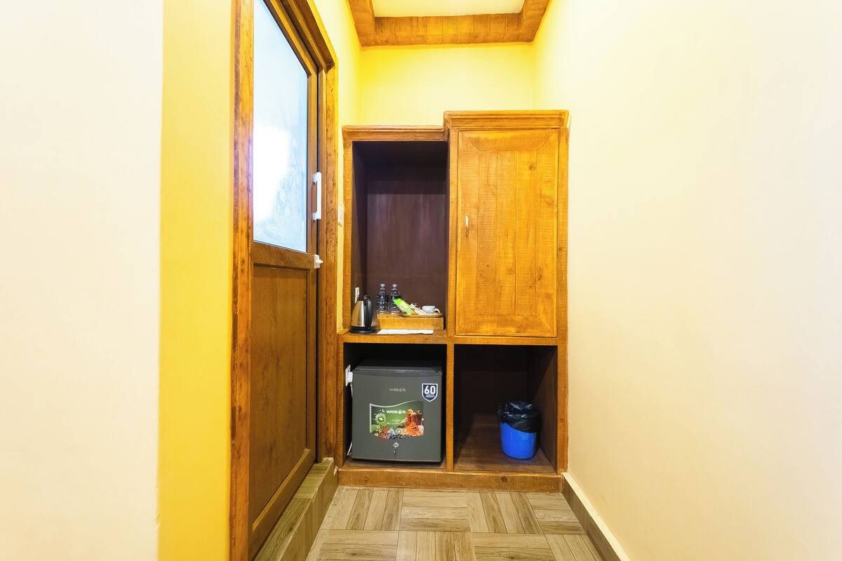 A compact room with a wooden cabinet, a small refrigerator, and a trash bin.