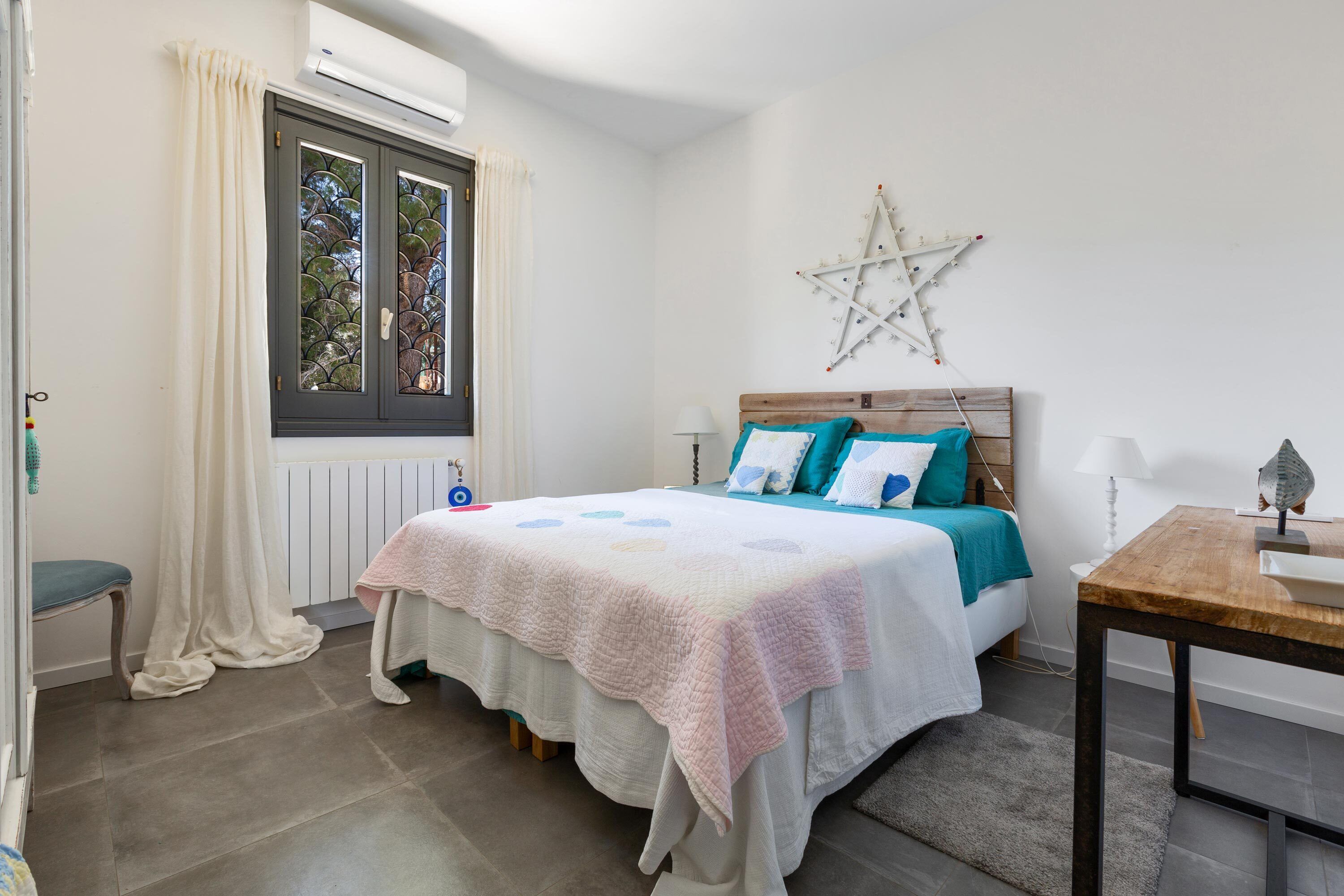 A bedroom with a bed, a star decoration on the wall, a window with curtains, and a bedside table.