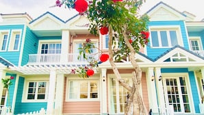 A two-story house with a white picket fence, a wooden ladder, and a tree with red flowers. - Holiday Villa Novaworld Phan Thiet (Tien Thanh)