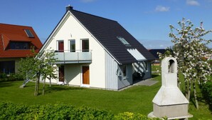A two-story house with a balcony, a small garden, and a stone monument. - Holiday Apartment Sandpiper Ground Floor (Klütz)