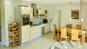 A modern kitchen with white cabinets, a built-in oven, and a dining area with wooden chairs and a table. - Holiday Apartment Sandpiper Ground Floor (Klütz)