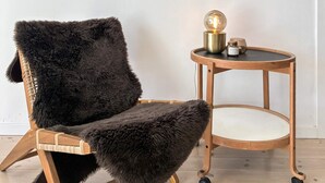 Ein Sessel mit fellbezogener Lehne und ein runder Holztisch mit einer Globenlampe.