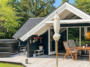 A modern outdoor deck with a hot tub, a table with chairs, and a covered seating area.