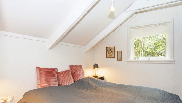 Ein Schlafzimmer mit einem Bett, einem Nachttisch, einer Lampe, einem Fenster und einer Deckenleuchte.