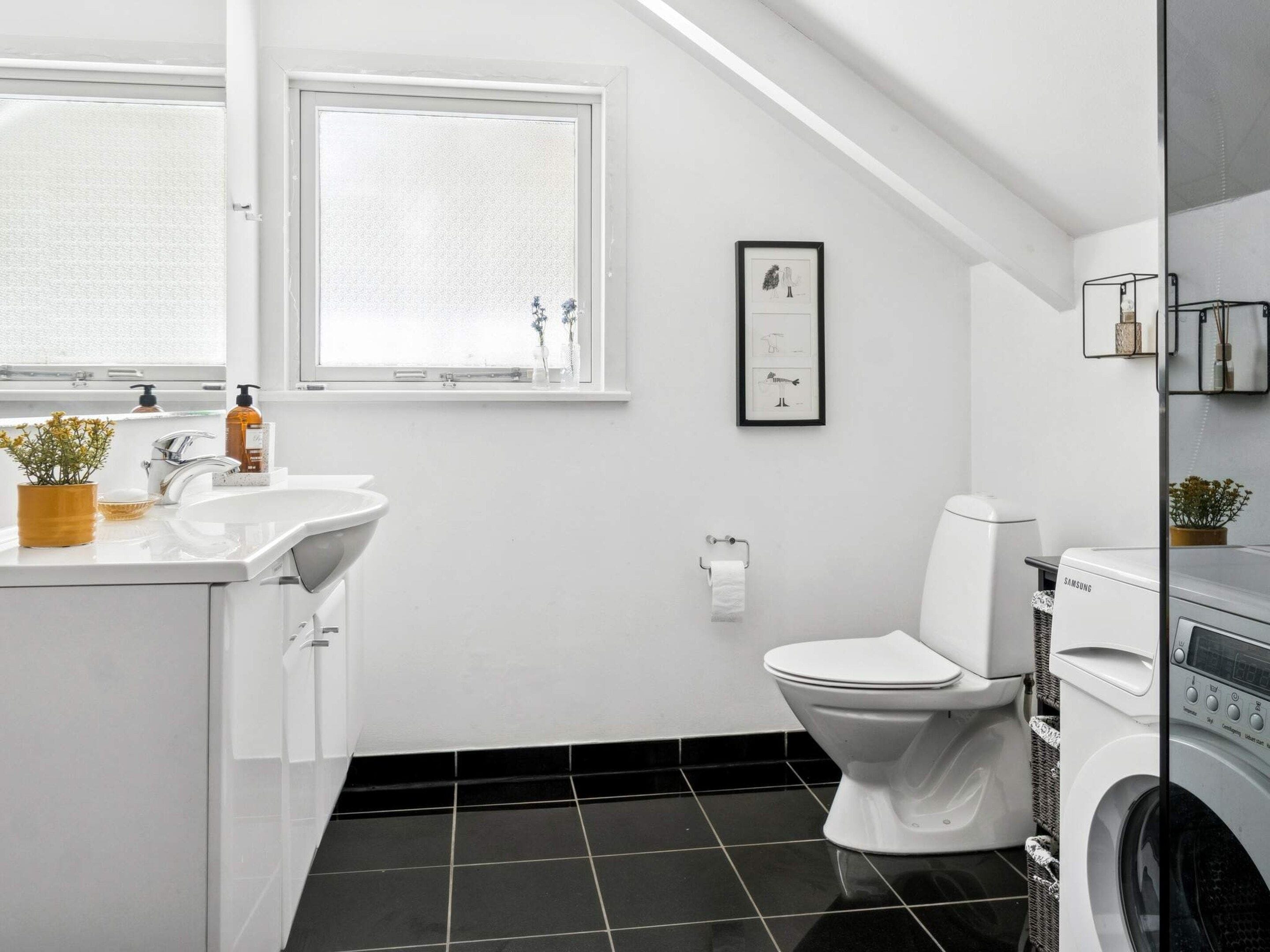 A modern bathroom with a white sink, toilet, and washing machine.