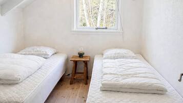 A small, clean room with two beds, a window with a view of trees, and a small wooden stool.