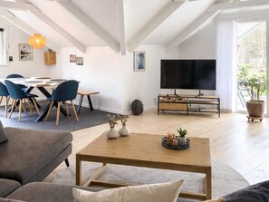 A living room with a sofa, coffee table, TV, and dining area with chairs and a table.