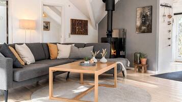A modern living room with a grey sofa, a wooden coffee table, a fireplace, and a large window.