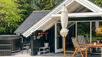 A modern outdoor deck with a hot tub, a table with chairs, and a covered seating area.
