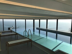 A modern infinity pool with a glass floor, two lounge chairs, and a view of a cityscape and water. - Apartment on the Beach in Sellin (Sellin)
