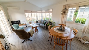 A spacious living room with a sofa, armchair, and dining table. There is a TV, a plant, and a window with curtains. - Canal-side Stay, Giethoorn (Giethoorn)
