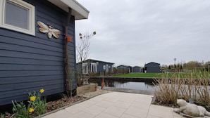A residential area with a paved walkway, a small pond, and houses with dark siding. - Canal-side Stay, Giethoorn (Giethoorn)